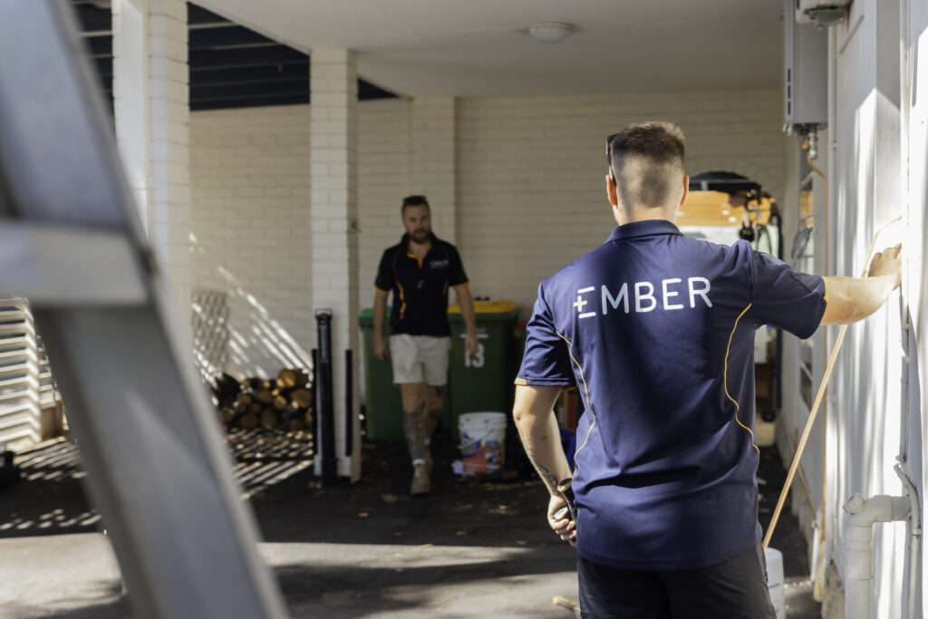 Two Ember workers in a service corridor, one wearing an Ember branded polo shirt, inspecting an exterior wall