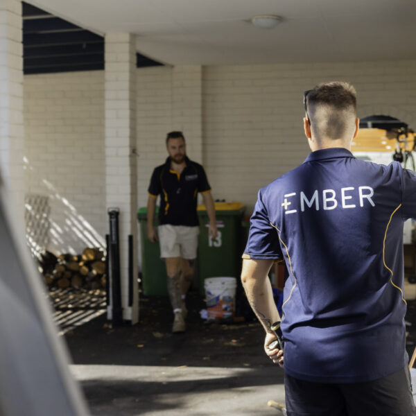 Two Ember workers in a service corridor, one wearing an Ember branded polo shirt, inspecting an exterior wall