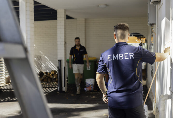 Two Ember workers in a service corridor, one wearing an Ember branded polo shirt, inspecting an exterior wall